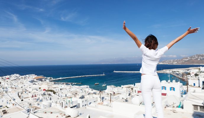 mykonosRear view of young woman with arms outstretched, looking at the cityscape of Mykonos island, Greece.