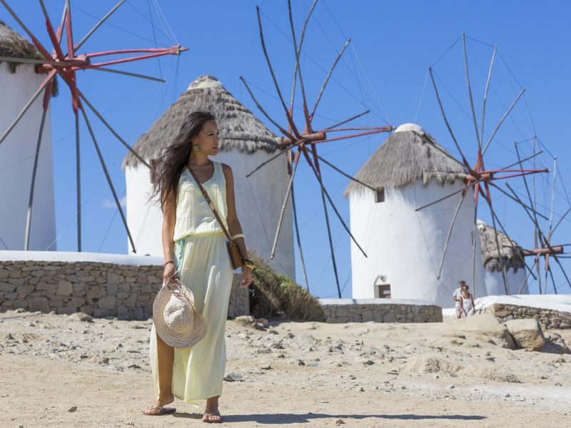 a beautiful girl posing in front of The Mykonos windmills, iconic feature of the Greek island of the Mykonos
