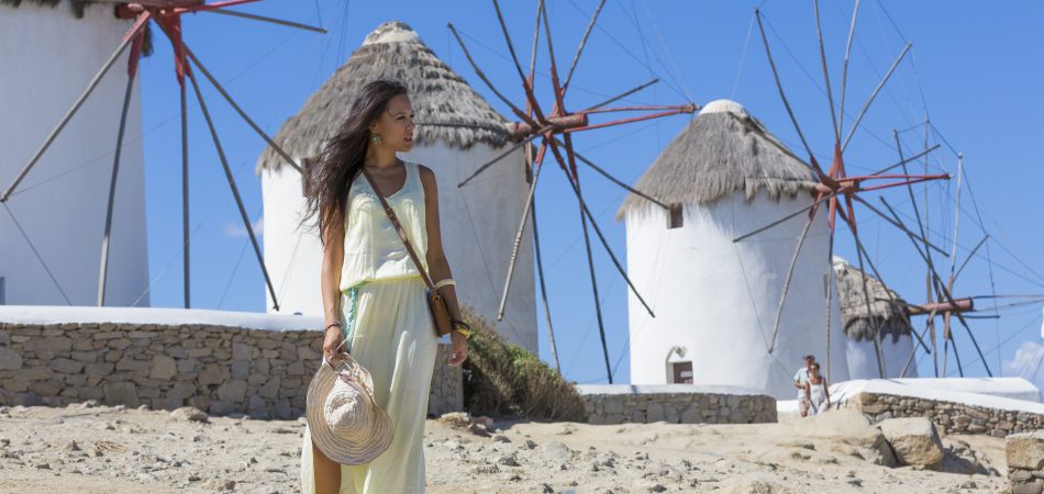 a beautiful girl posing in front of The Mykonos windmills, iconic feature of the Greek island of the Mykonos